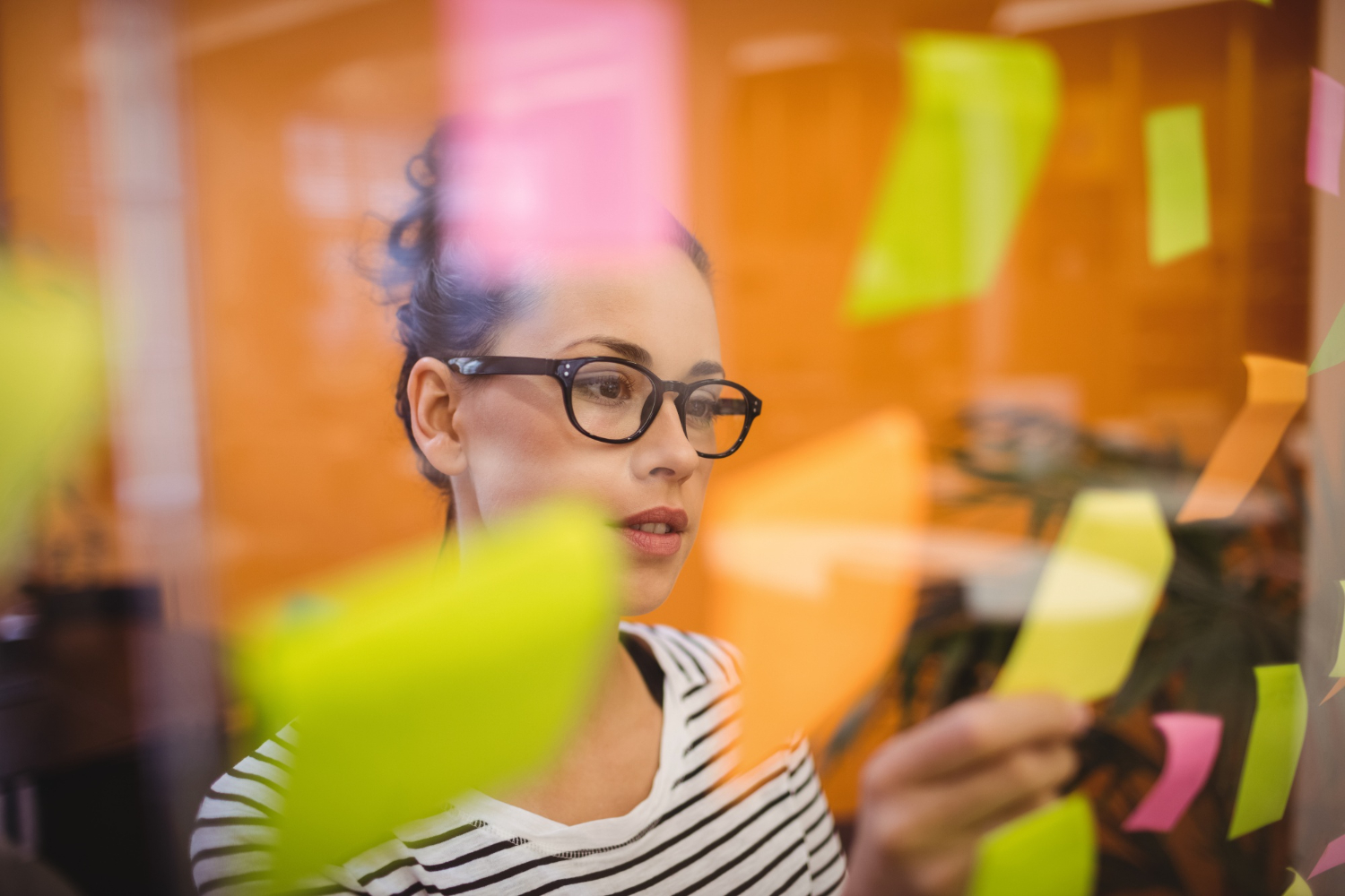 donna che legge un post-it tra tanti appesi su una parete trasparente